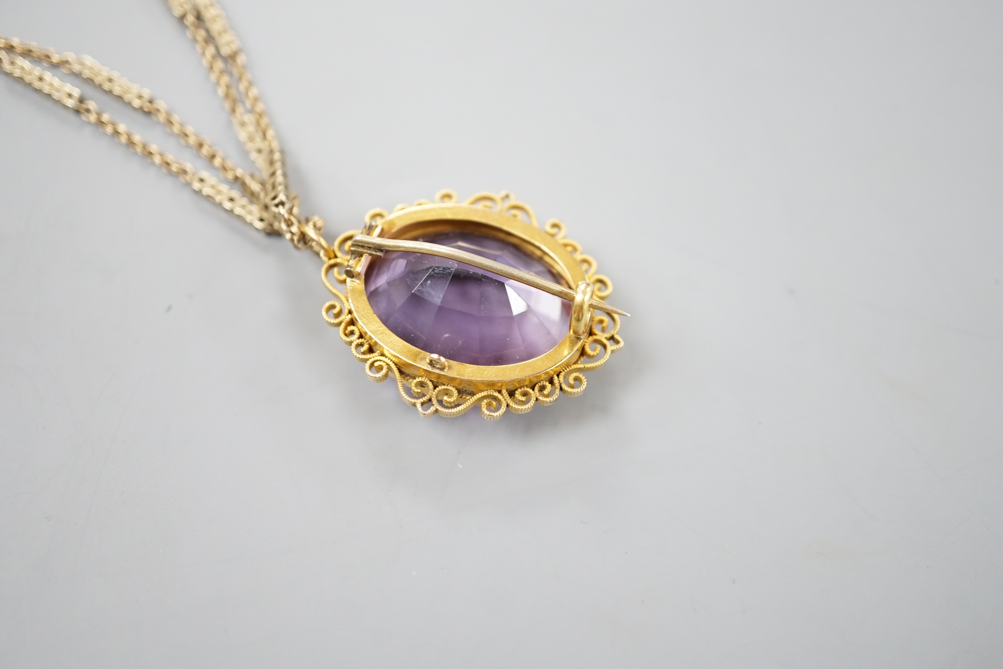 A yellow metal mounted oval cut amethyst pendant brooch, 34mm, gross 13.2 grams, on a Victorian pinchbeck guard chain, 70cm.